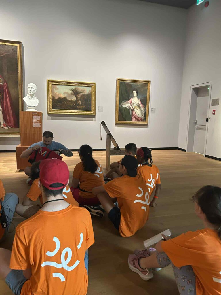 Jeunes assis au sol dans une salle de musée devant des tableaux de Napoléon.