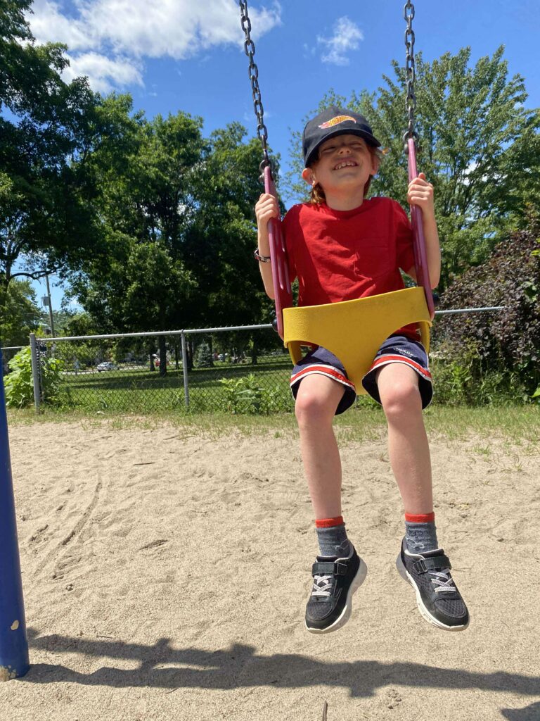Petit jeune se balançant heureux dans une balançoire pour bébé, dans un parc l'été.