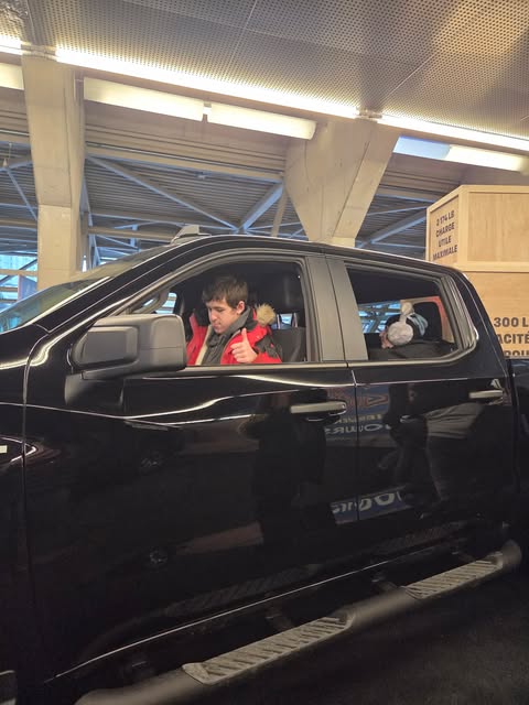 Jeune testant le confort d'une voiture au Salon de l'auto, assis sur le banc avant en faisant un signe qu'il est content.
