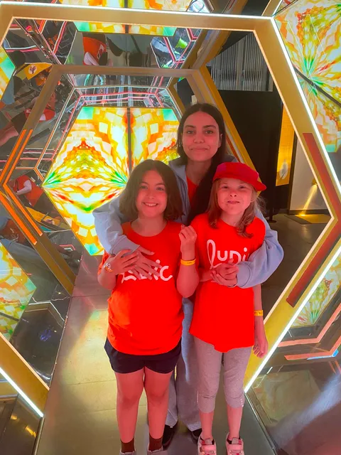 Deux jeunes campeuses avec leur accompagnatrice dans un tunnel de miroir au Centre des Sciences, souriant.