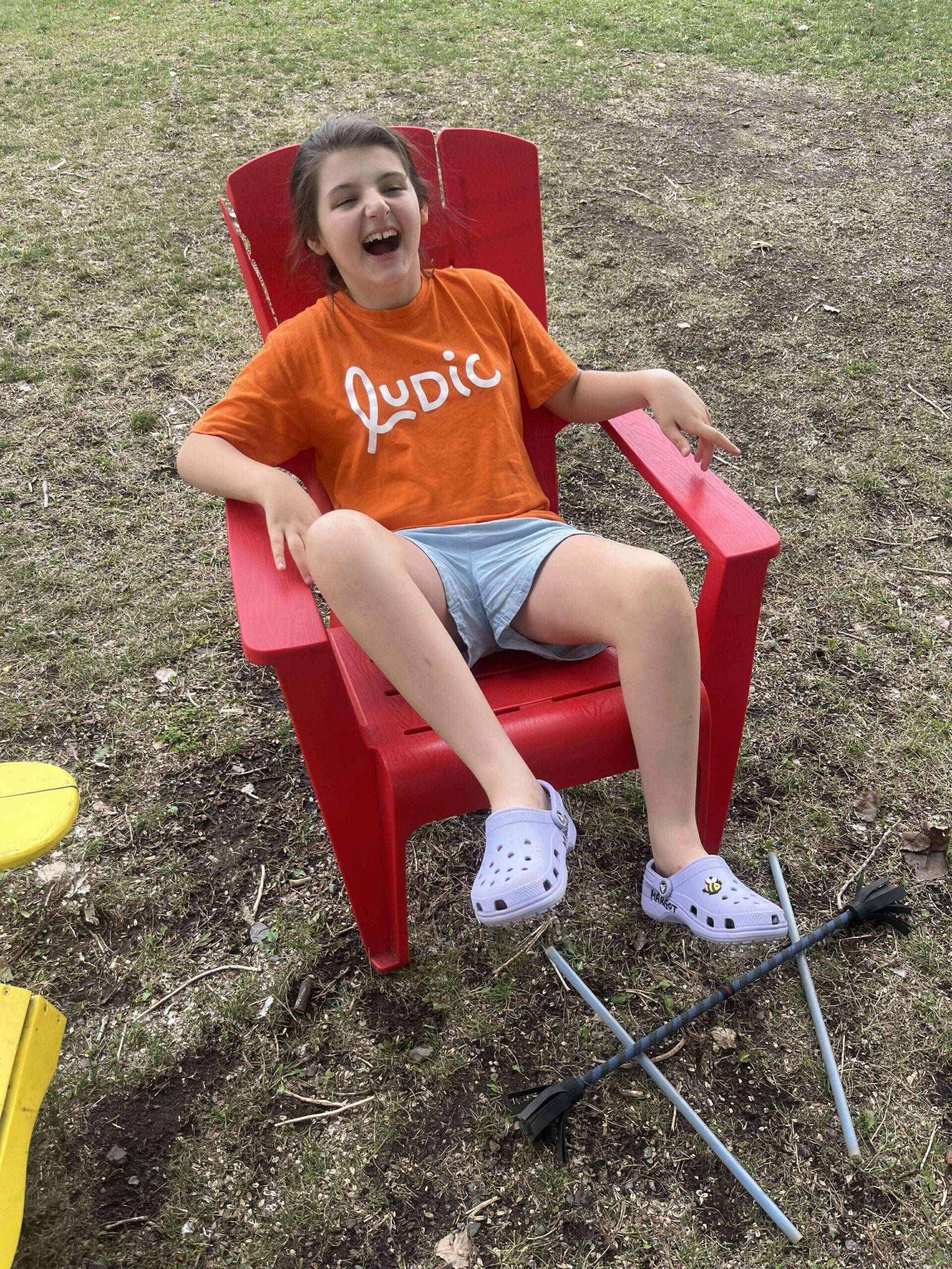 Jeune souriante assise sur une chaise rouge à l'extérieur